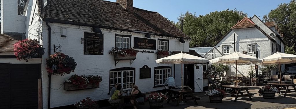 The White Horse at Longford, its white painted frontage with hanging baskets and parasols outside