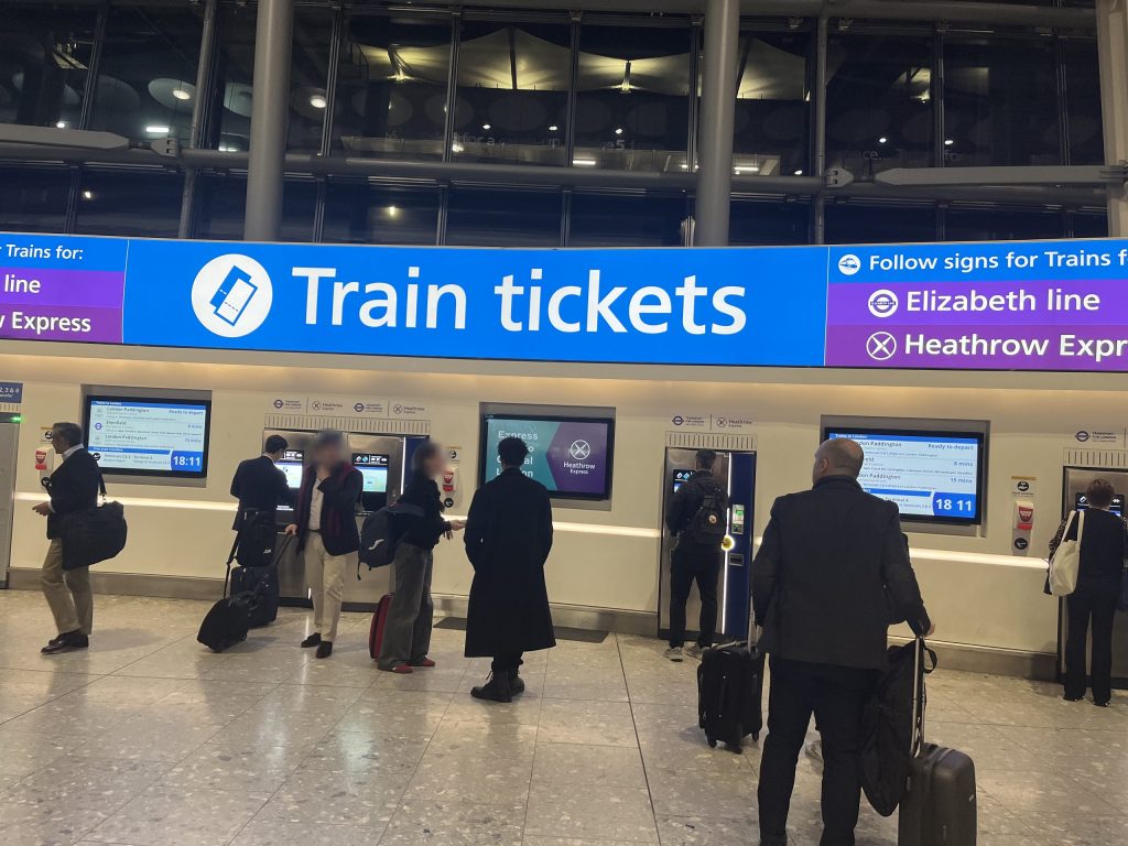 Passengers at the Heathrow train ticket machines under the Train tickets sign, with signs for the Elizabeth line and Heathrow Express