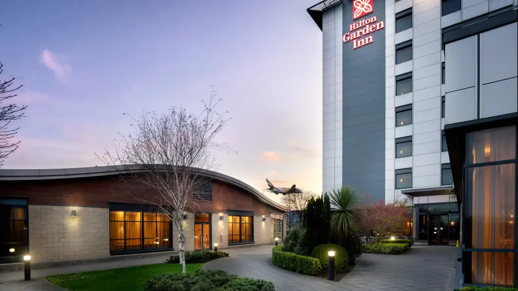 The Hilton Garden Inn at Hatton Cross at dusk, with the lit tower sign and a curved single-storey wing