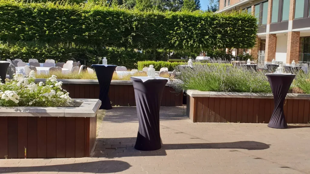 Outdoor terrace at the Hilton London Heathrow Terminal 5, set up with tall tables beside a hedge