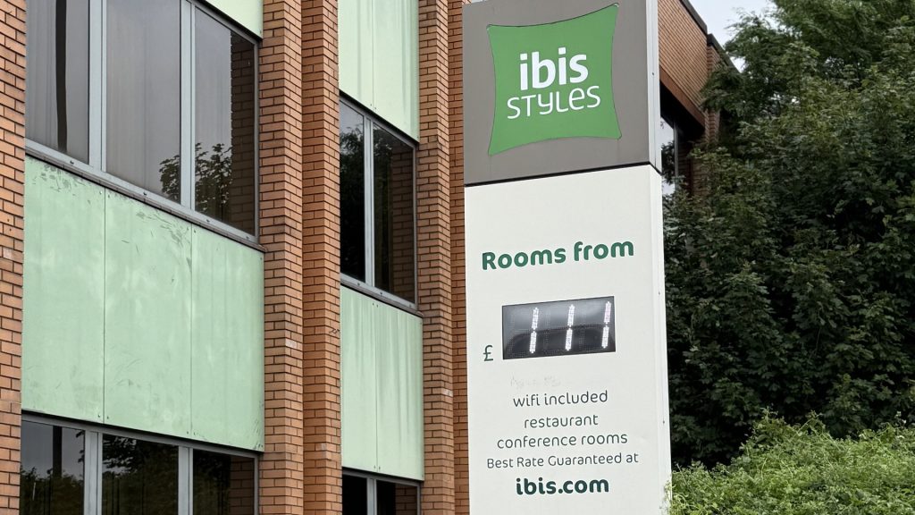 The ibis Styles Heathrow totem sign on Bath Road, with the green cladding and brick of the hotel behind it