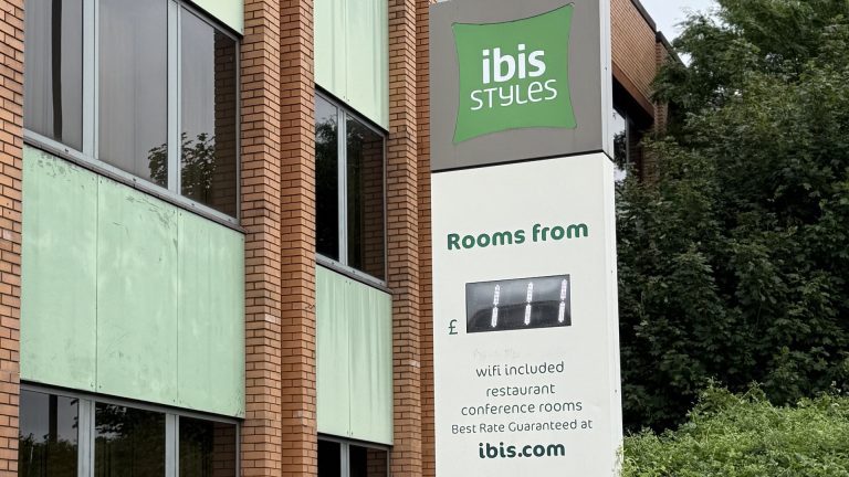 The ibis Styles Heathrow totem sign on Bath Road, with the green cladding and brick of the hotel behind it