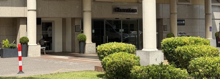 The Sheraton Heathrow entrance, with the hotel name above the doors under the columned portico