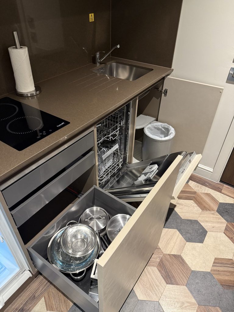 A kitchen drawer open, showing the crockery and the dishwasher below